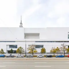 Nowoczesny, biały budynek muzeum w Warszawie z czerwonym autobusem i samochodami na ulicy.